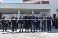 A képen egy szalagátvágási ceremónia látható, ahol több hivatalos öltözetben lévő férfi vesz részt.