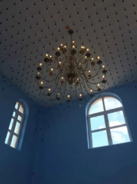 A képen egy magas, világoskék falú terem látható, amelynek mennyezetén egy nagyméretű,c sillár függ.